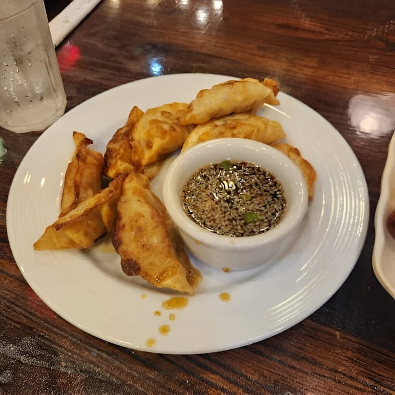 A plate of golden-brown fried dumplings with a side of dipping sauce at New Hong Kong House.
