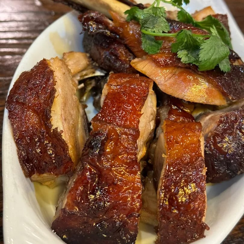 Close-up of crispy roasted duck pieces garnished with fresh cilantro on a white plate.