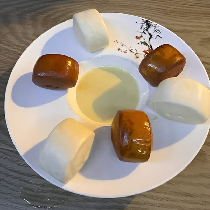 A white plate with six Chinese steamed buns, three white and three golden brown, surrounding a dipping sauce.